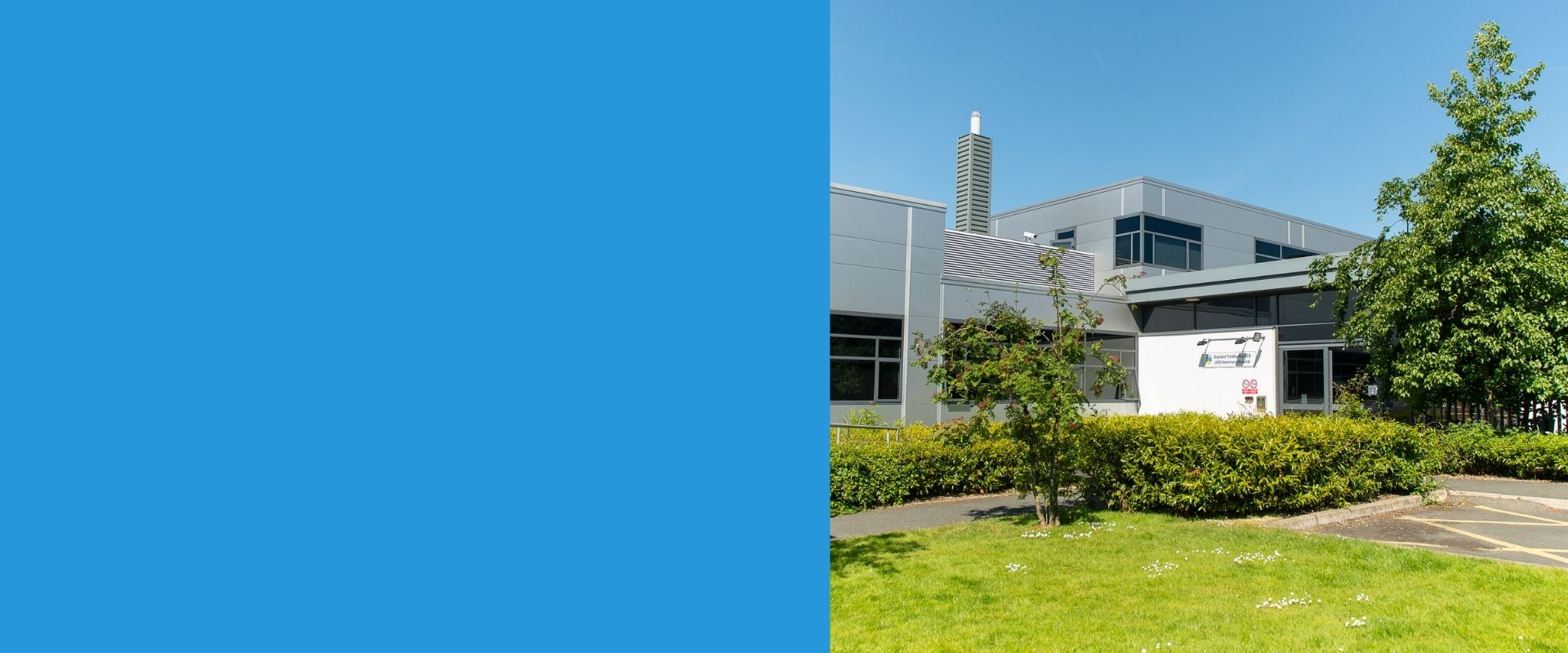Exterior view of the UCD Veterinary Hospital on a sunny day, showing a modern grey building surrounded by landscaped greenery and trees on the Belfield campus.